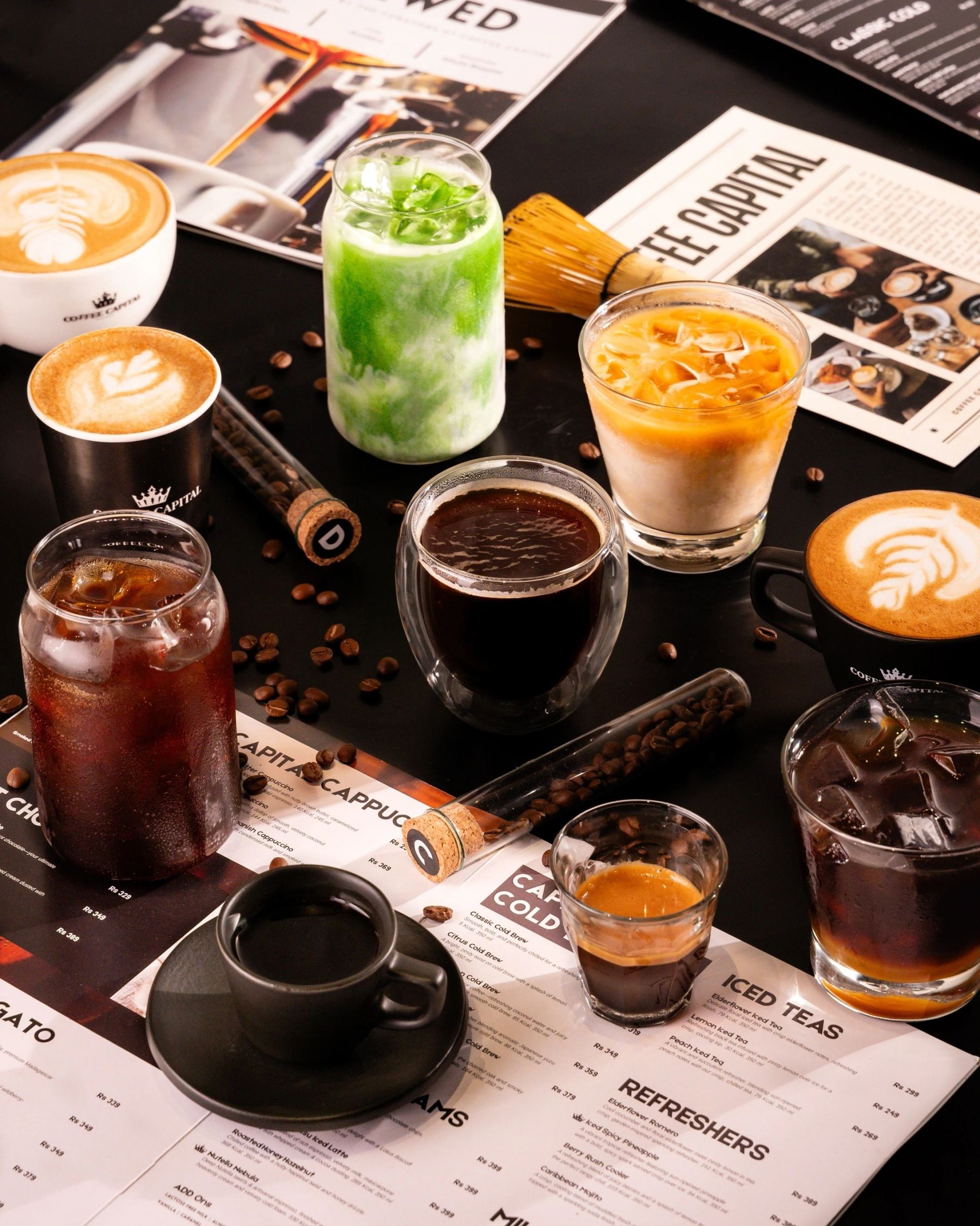 A real spread of Coffee Capital drinks — cold brews, cappuccino, affogato — with menu cards and coffee beans